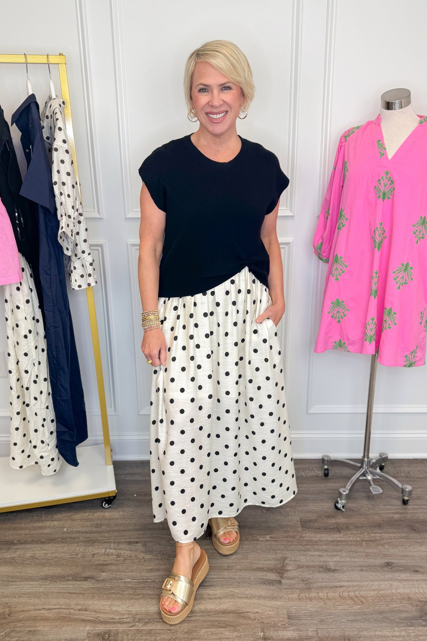 Front view of woman wearing Swagger Boutique’s Black &amp; Cream Polka Dot Layered Midi Dress by Entro with sandals at the store. 