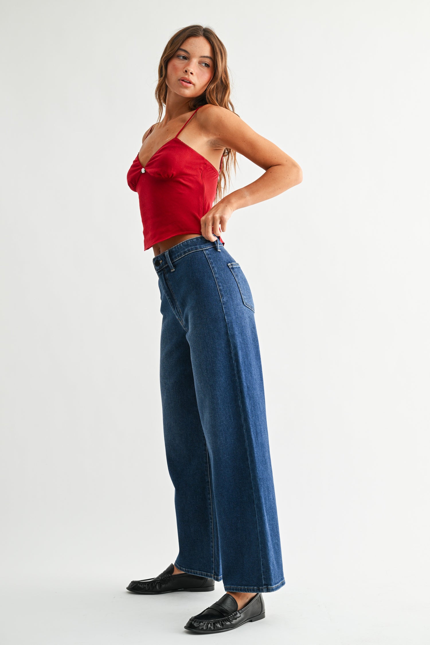 Side view of woman wearing red top with Dark Wash No Pocket Trouser Jeans against white studio background.