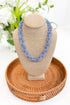 Blue necklace on a beige bust with a woven basket and blurred greenery in the background