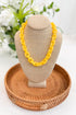Yellow necklace on a beige mannequin head with a woven basket and blurred flowers in the background