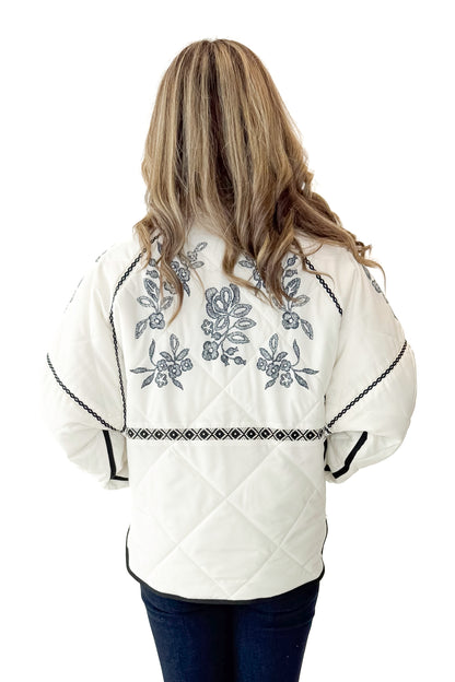 Back view of woman wearing Cream &amp; Navy Embroidery Print Puffer Jacket with jeans against white studio background.