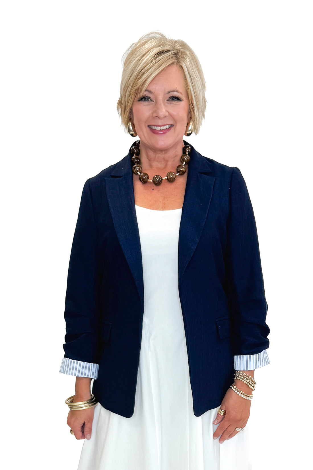Front view of woman wearing Navy Cinched Sleeve Blazer by Skies Are Blue with white dress against white studio background.