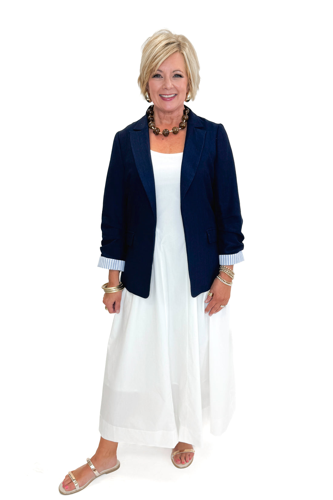 Front view of woman wearing Navy Cinched Sleeve Blazer by Skies Are Blue with white dress against white studio background.