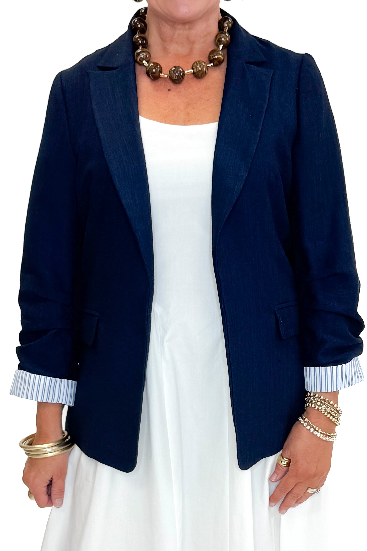 Front detail view of woman wearing Navy Cinched Sleeve Blazer by Skies Are Blue with white dress against white studio background.