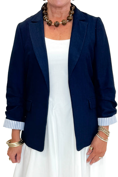 Front detail view of woman wearing Navy Cinched Sleeve Blazer by Skies Are Blue with white dress against white studio background.