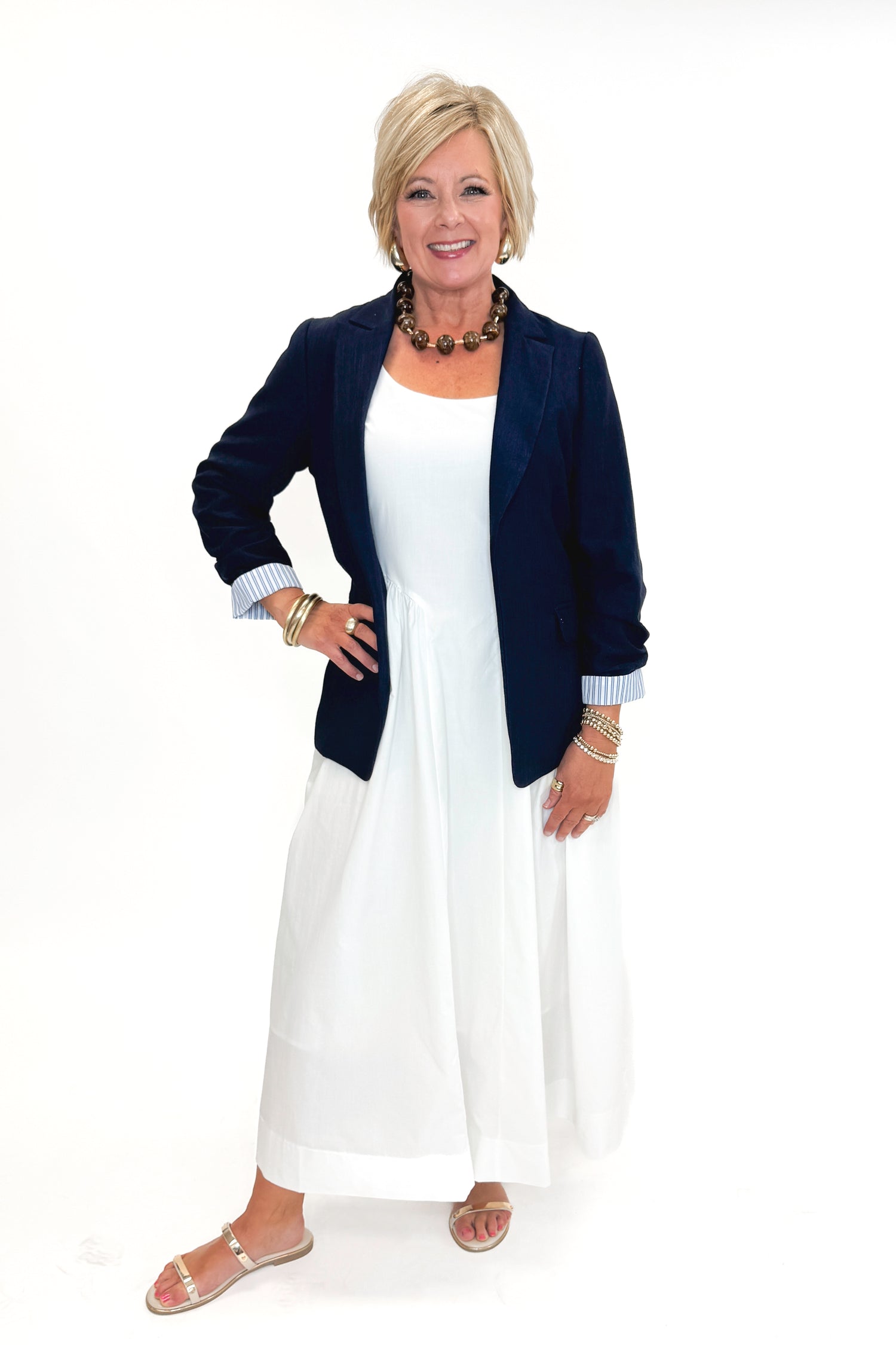 Front view of woman wearing Navy Cinched Sleeve Blazer by Skies Are Blue with white dress against white studio background.