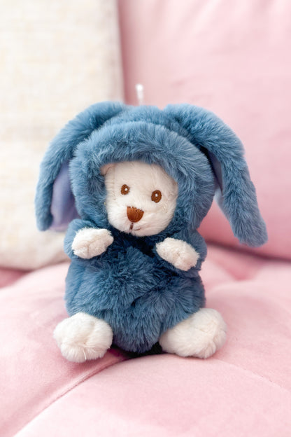 Stuffed animal in a blue bunny costume sitting on a pink surface