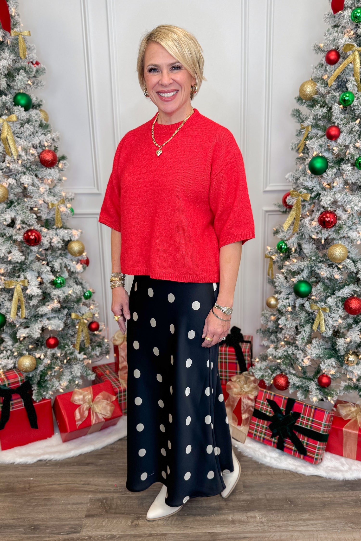 Woman in red top and polka dot pants standing between two decorated Christmas trees.