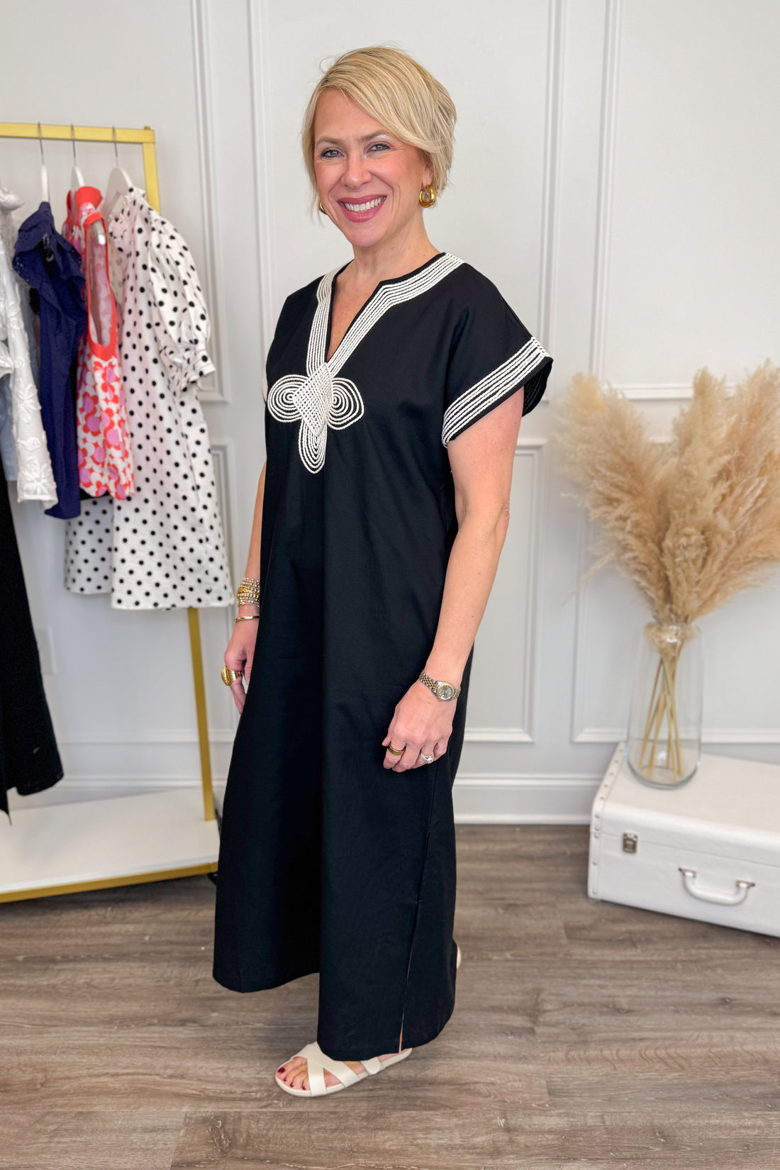 Woman wearing a black dress with white accents in a room with a clothing rack and decorative elements.