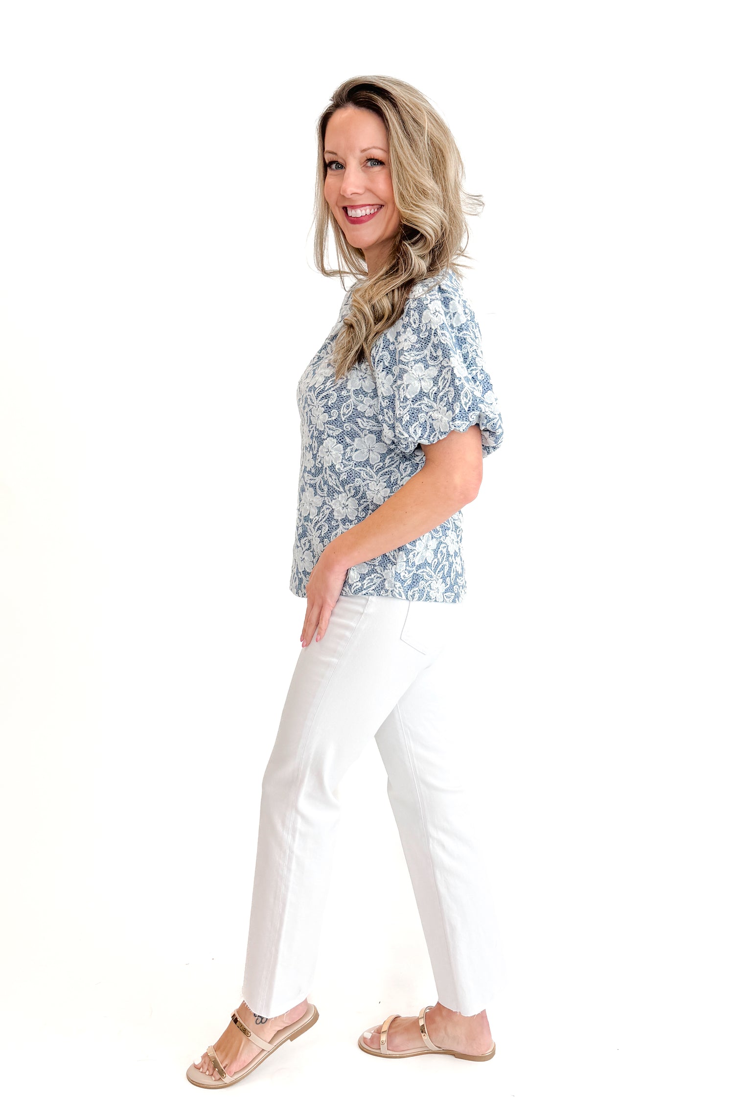 Side view of woman wearing Light Blue Floral Textured Top with jeans against white studio background.