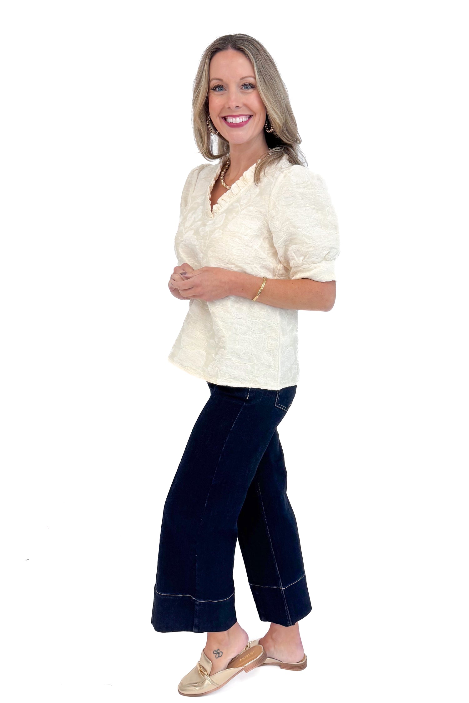 Side view of woman wearing Cream Floral Textured V-neck Top and blue jeans. 