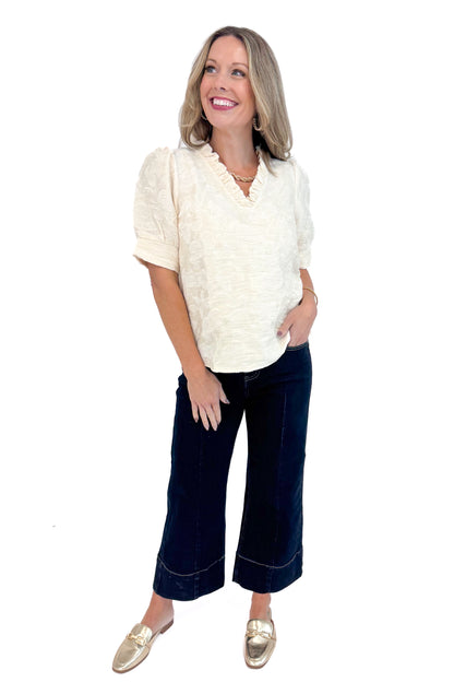 Front view of woman wearing Cream Floral Textured V-neck Top and blue jeans. 