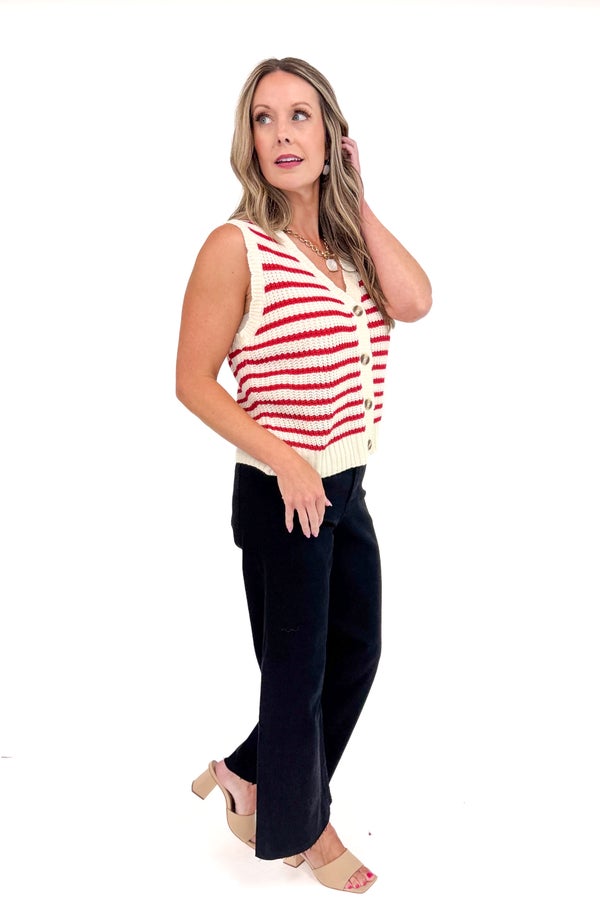 Woman wearing a red and white striped sleeveless sweater with black pants on a white background