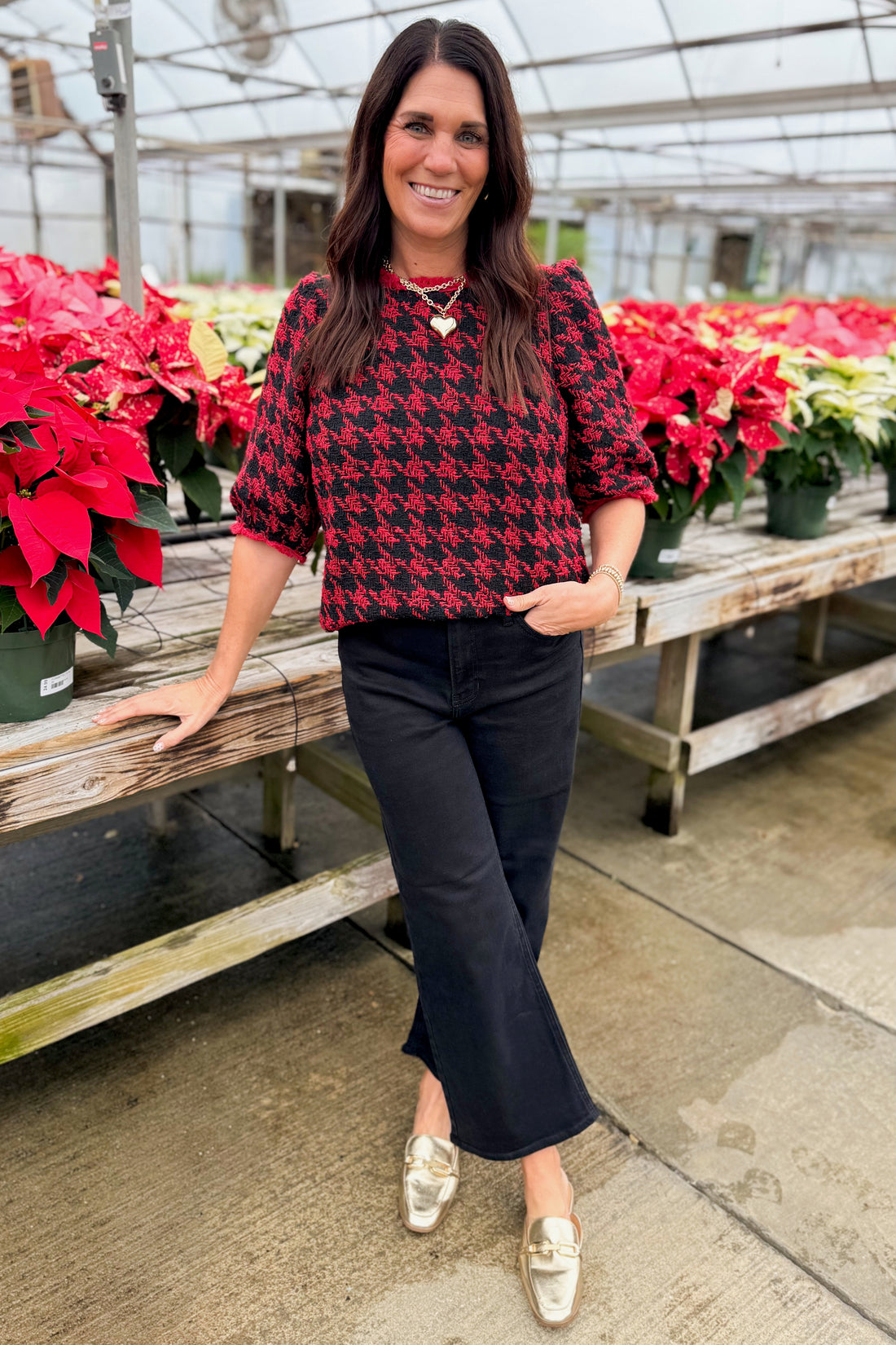 Woman in a red and black patterned top and black pants standing in front of decorations.
