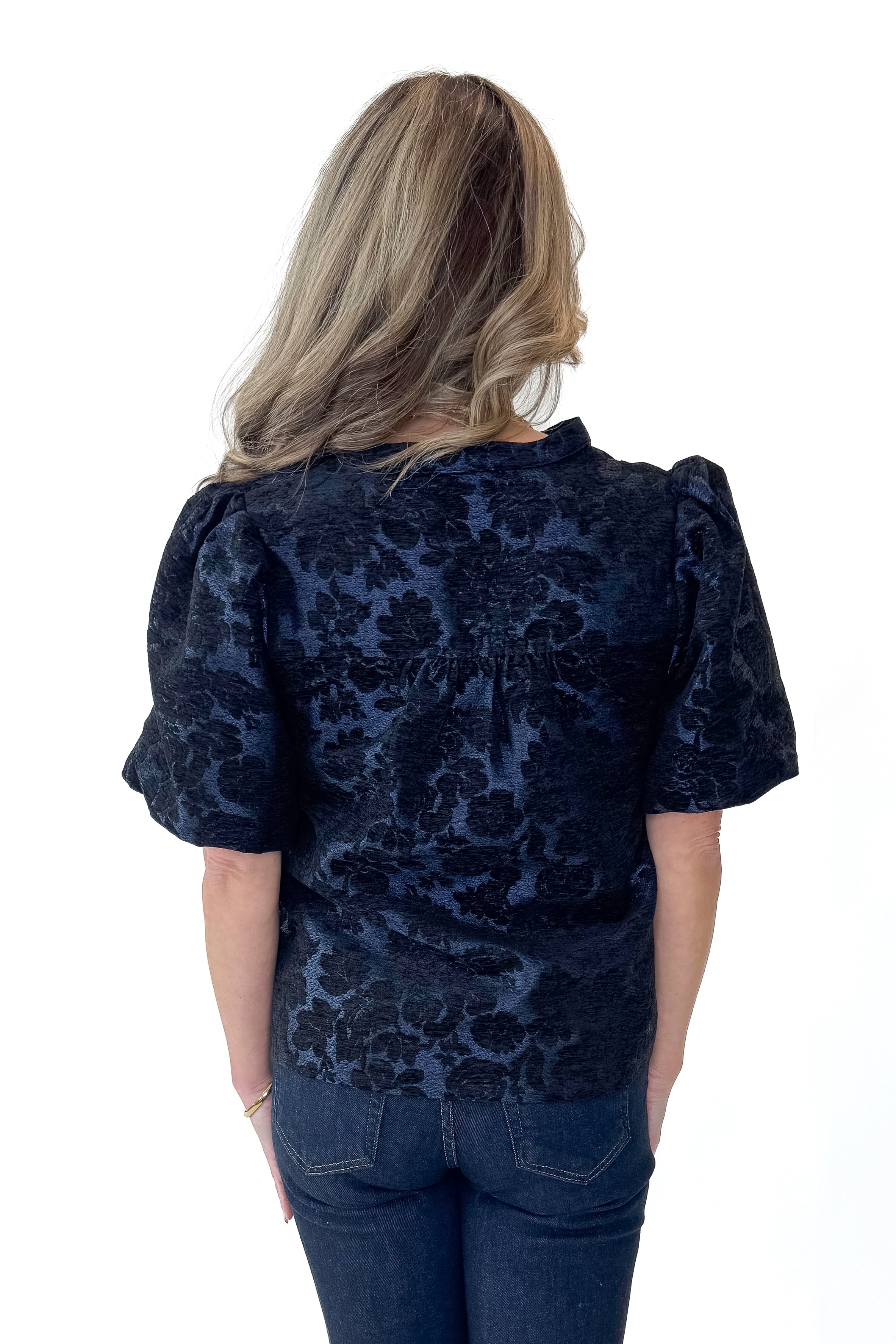 Back view of woman wearing Navy Floral Velvet Jacquard Top with jeans against white studio background.
