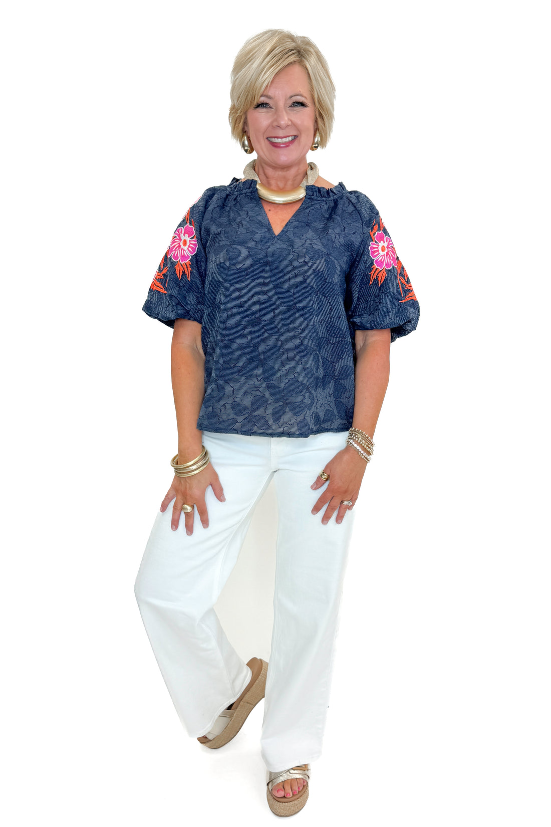 Front view of woman wearing Navy With Floral Embroidered Sleeve Top with jeans against white studio background.