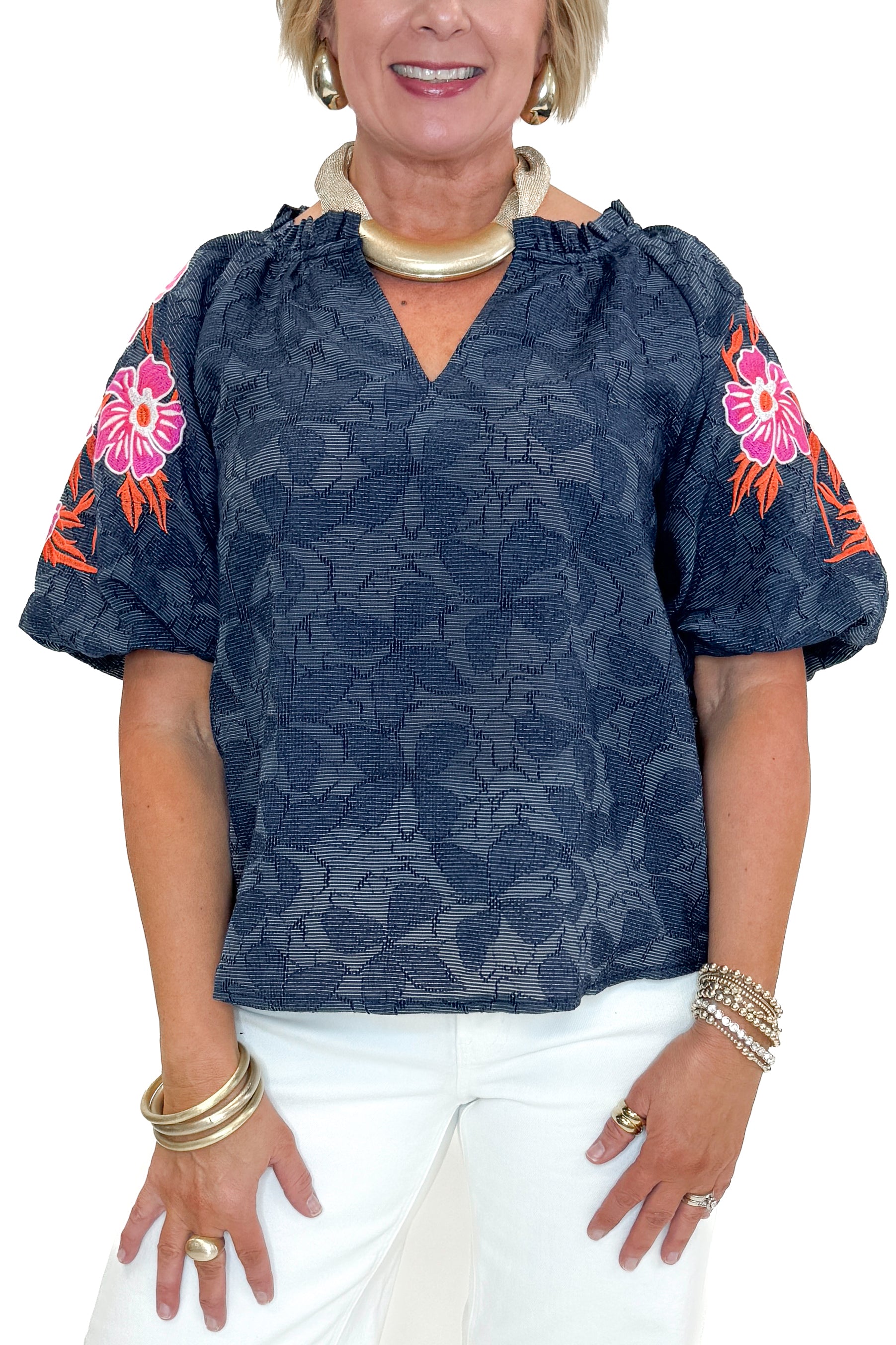 Front detail view of woman wearing Navy With Floral Embroidered Sleeve Top with jeans against white studio background.