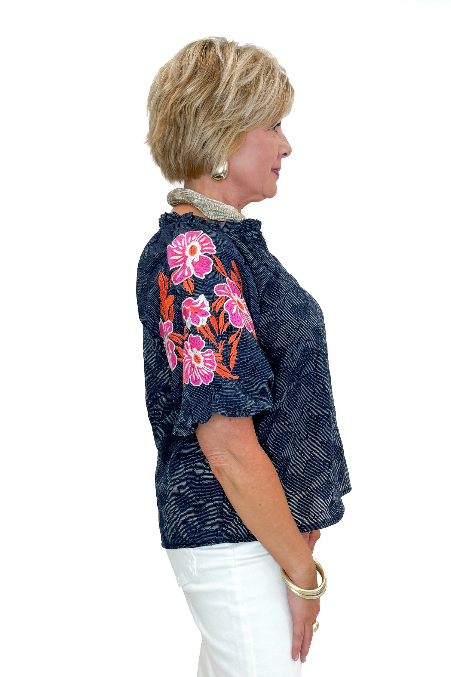 Side view of woman wearing Navy With Floral Embroidered Sleeve Top with jeans against white studio background.