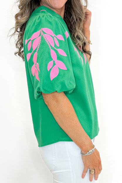 Side detail view of woman wearing Green &amp; Pink Floral Embroidered V-Neck Top with jeans against white studio background.