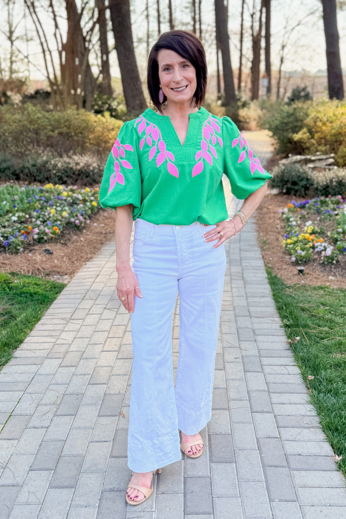 Front view of woman wearing Green &amp; Pink Floral Embroidered V-Neck Top with jeans at a garden outside.