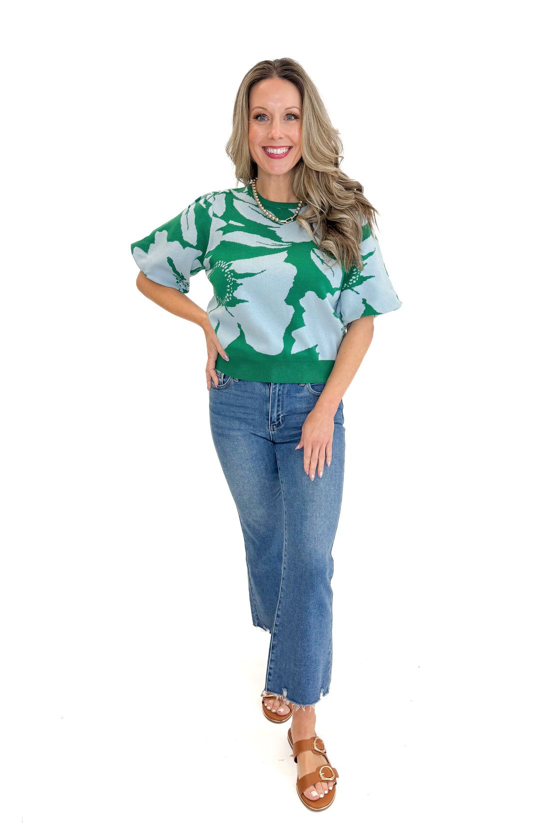 Front view of woman wearing Green &amp; Blue Floral Printed Short Sleeve Sweater with jeans against white studio background.