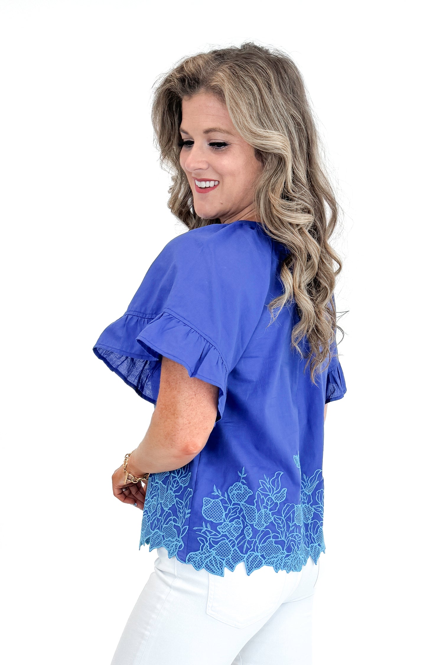 Side view of woman wearing Blue Embroidered Hem Top with jeans against white studio background.