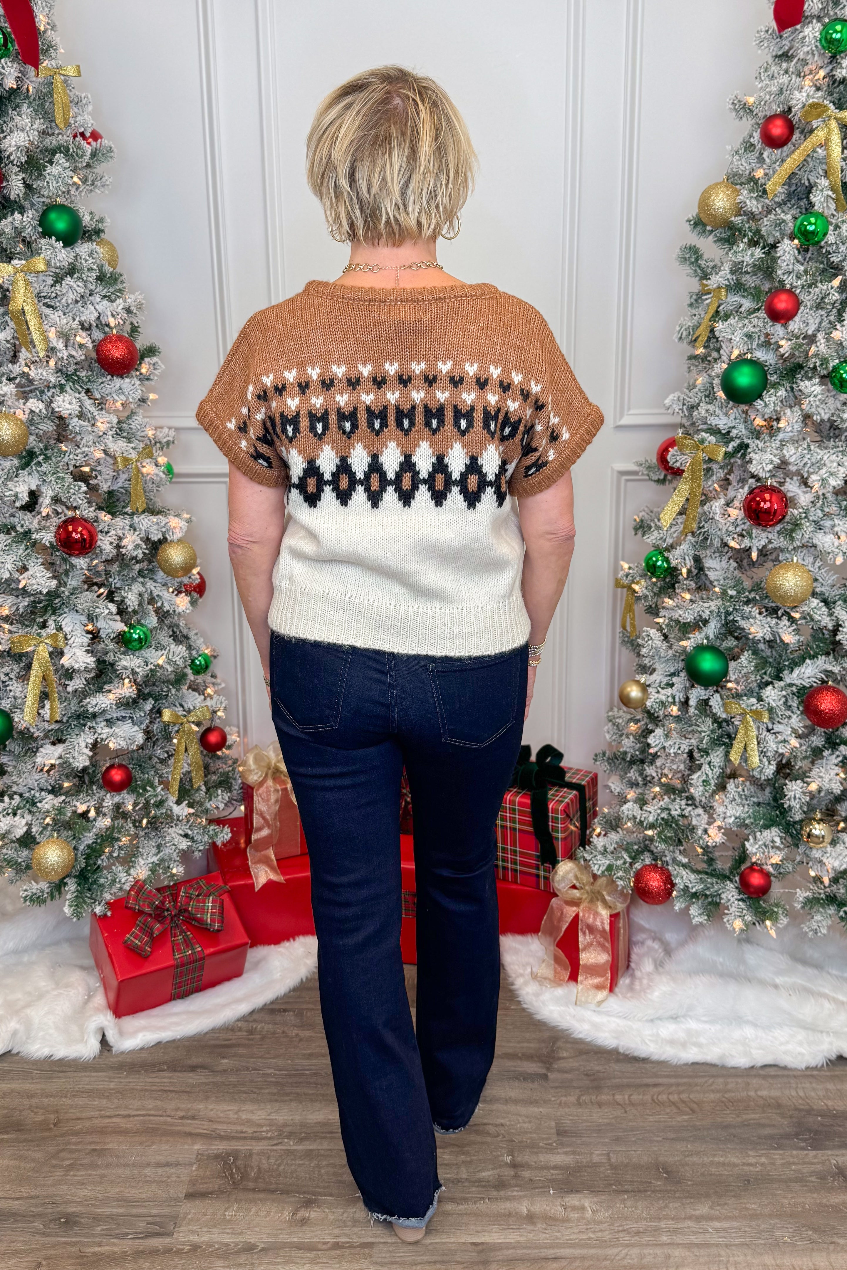 Person wearing a patterned sweater standing in front of Christmas trees with decorations.