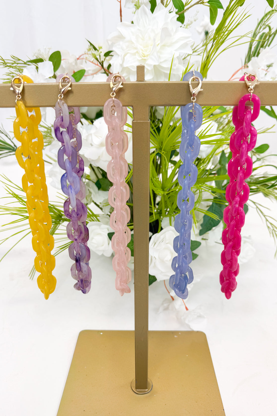 Colorful chain-style necklaces on a stand with a floral background