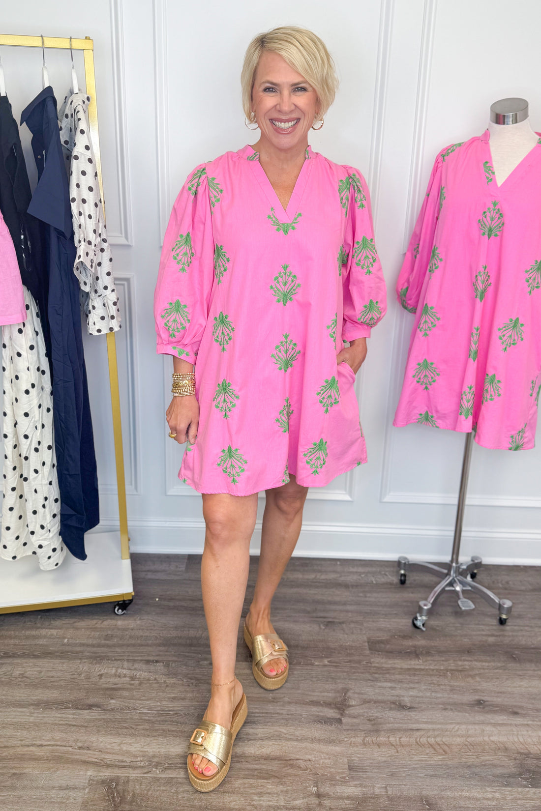 Front view of woman wearing Swagger Boutique’s Pink &amp; Green 3/4 Sleeve Embroidered Dress with sandals with clothes around her.