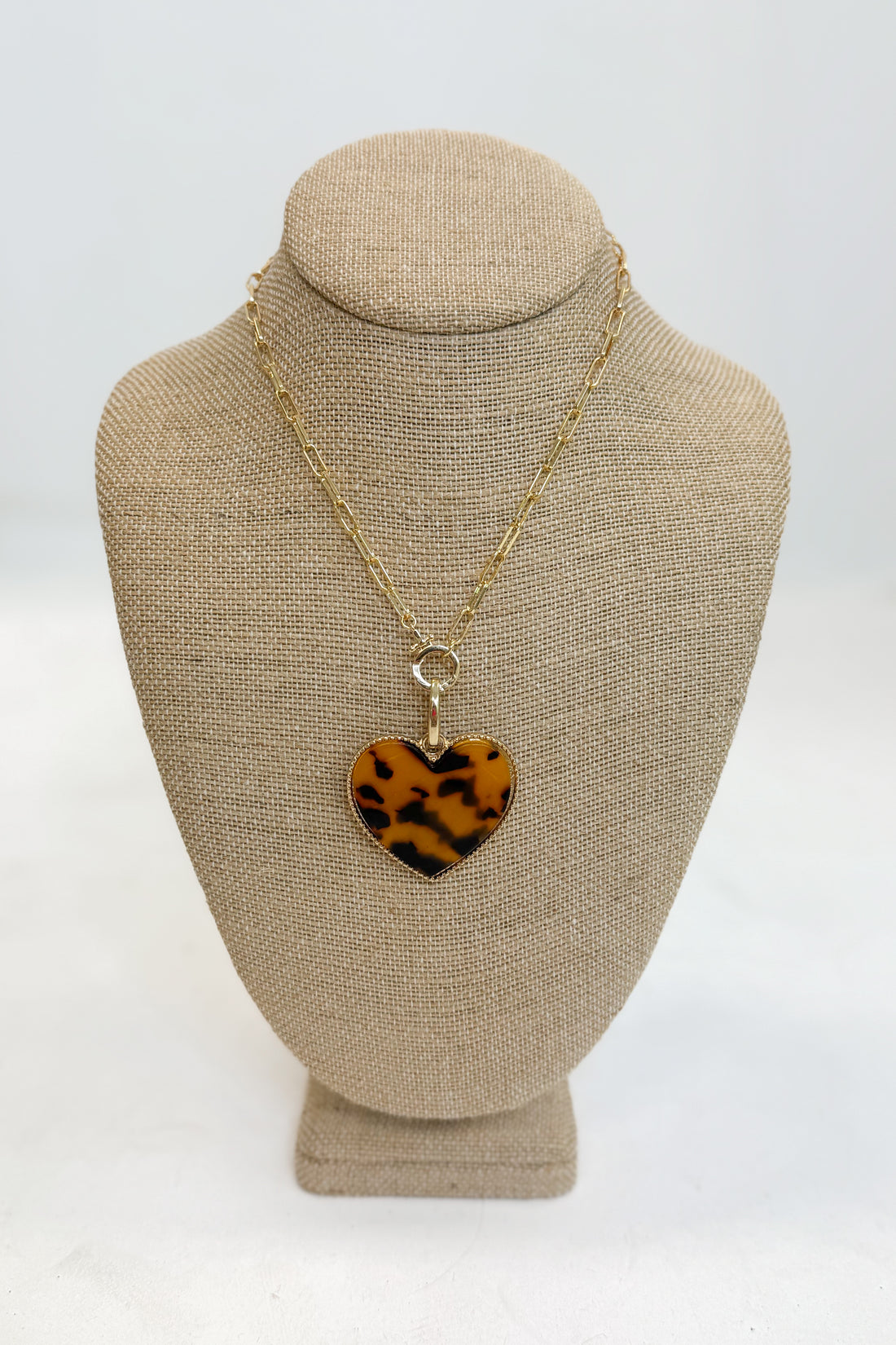 Necklace with a heart-shaped leopard print pendant on a beige bust against a white background