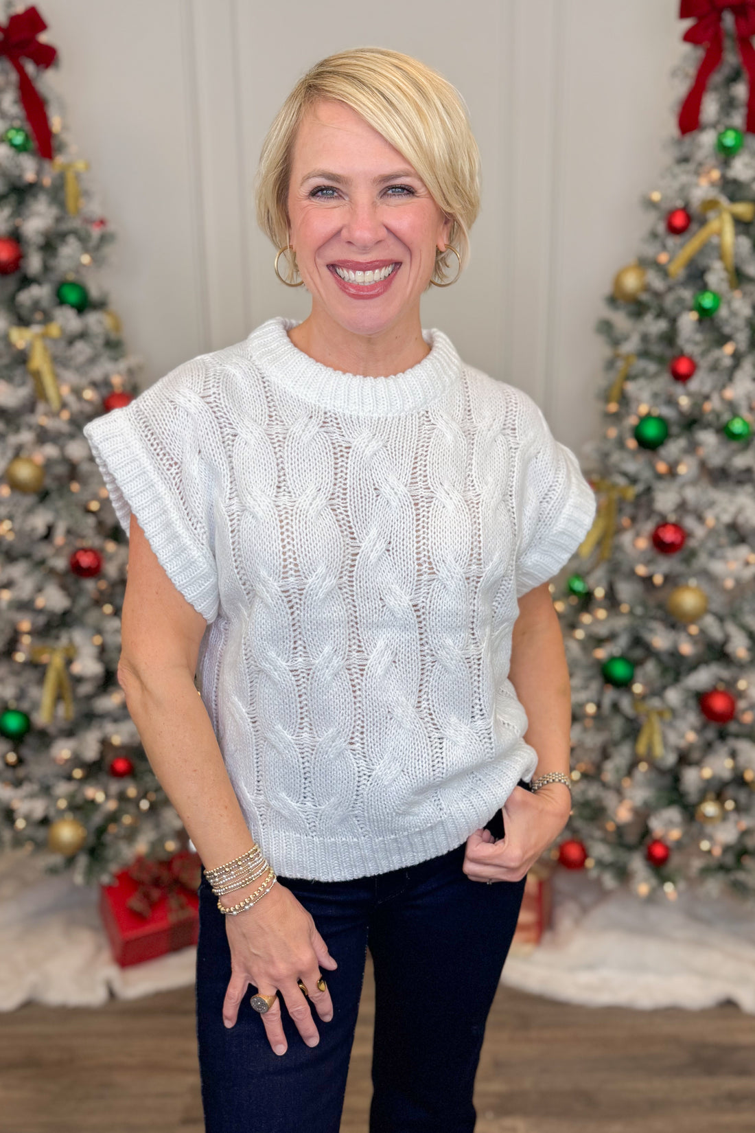 Woman wearing a white sweater in front of Christmas trees