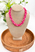 Necklace on a beige mannequin bust with a woven basket and blurred greenery in the background