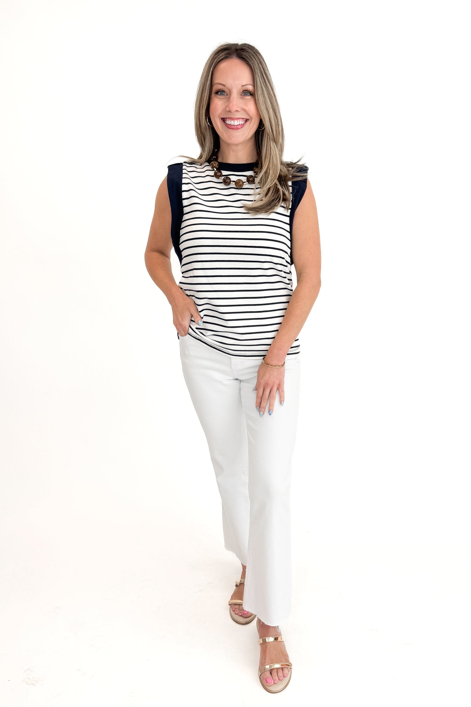 Front view of woman wearing White &amp; Navy Striped Sleeveless Top with white jeans against white studio background.