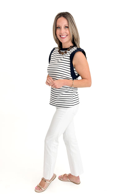 Side view of woman wearing White &amp; Navy Striped Sleeveless Top with white jeans against white studio background.