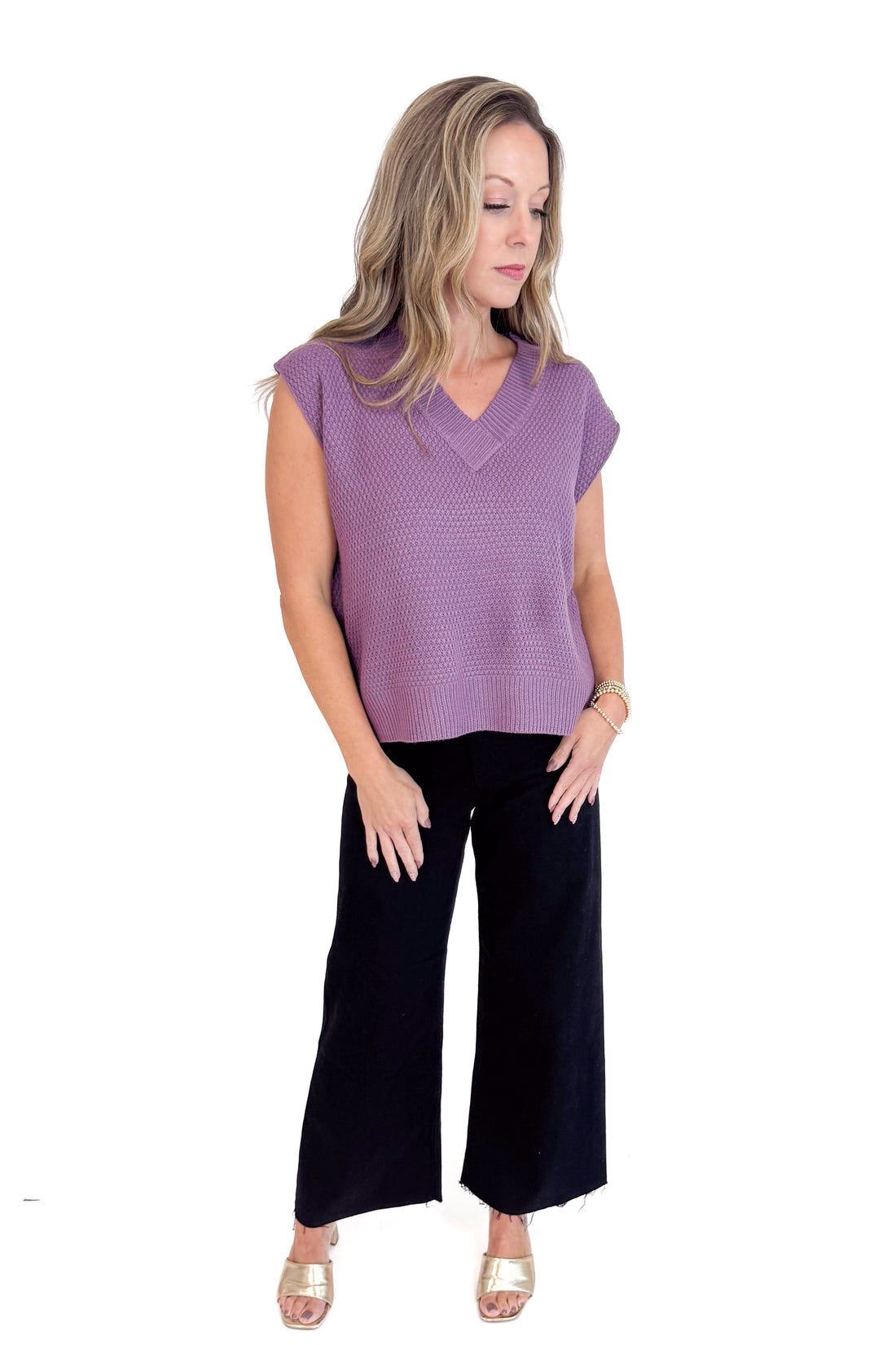 Woman wearing a purple sleeveless top and black pants on a white background