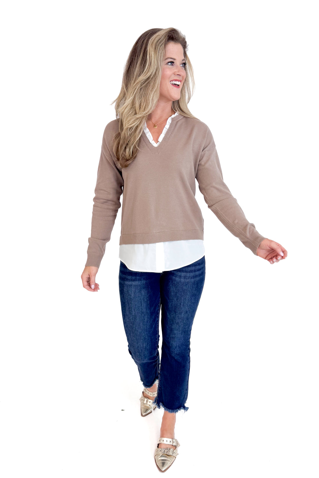 Woman wearing a brown sweater, white shirt, and blue jeans on a white background