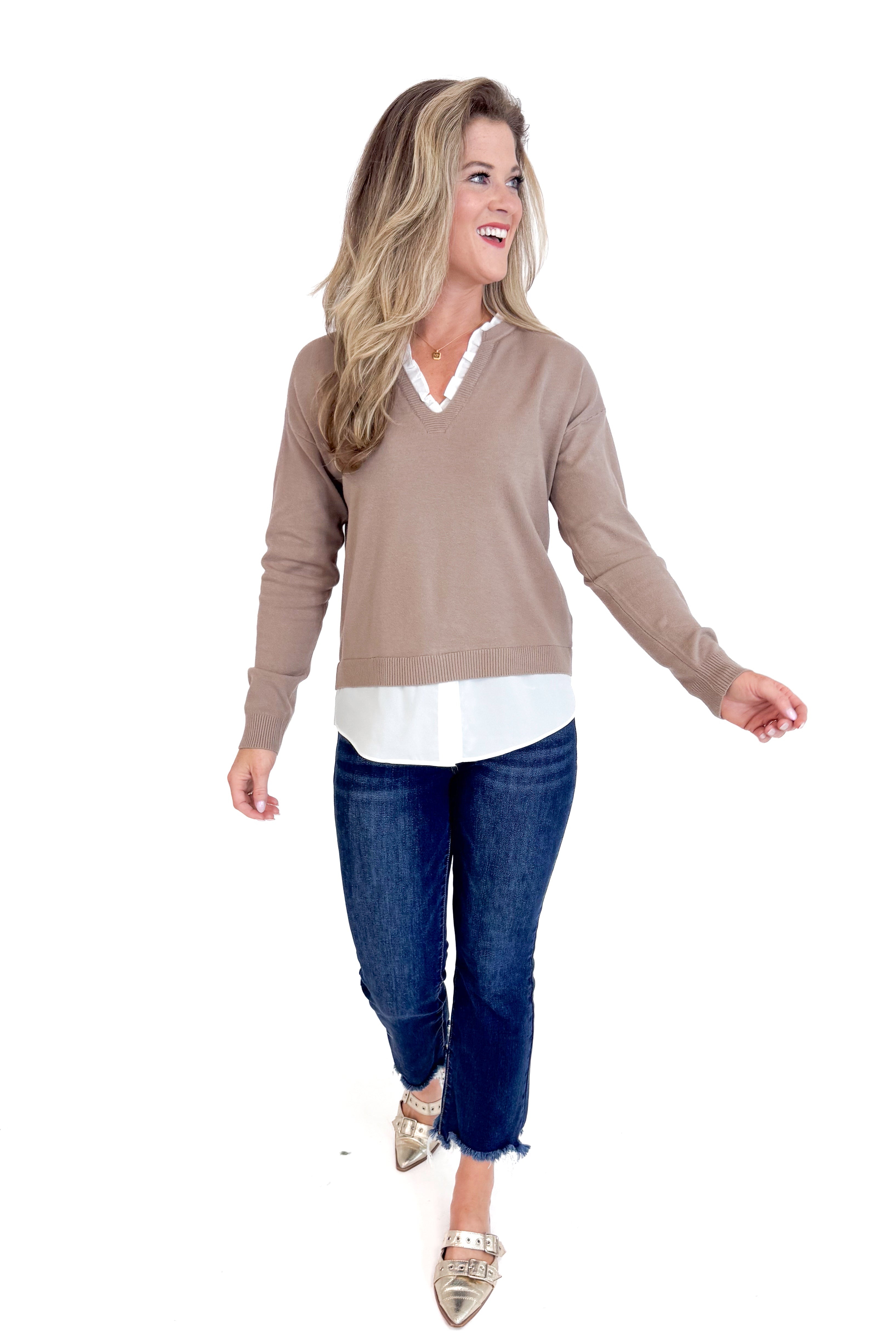 Woman wearing a brown sweater, white shirt, and blue jeans on a white background