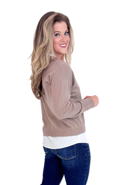 Woman wearing a brown sweater over a white shirt with blue jeans on a white background