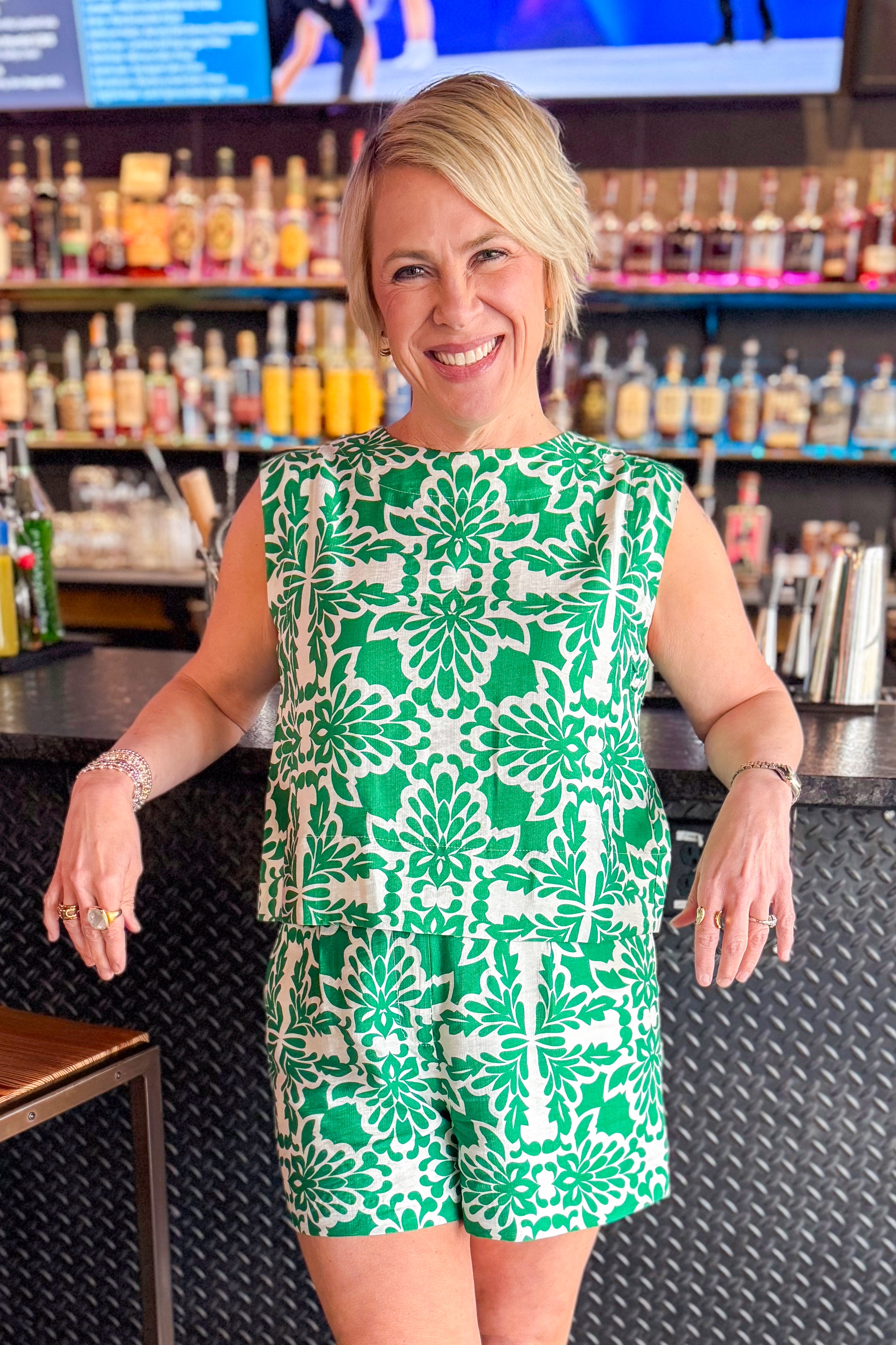 Front view of woman wearing Green &amp; Ivory Printed Tank by Skies Are Blue with matching shorts at a bar.