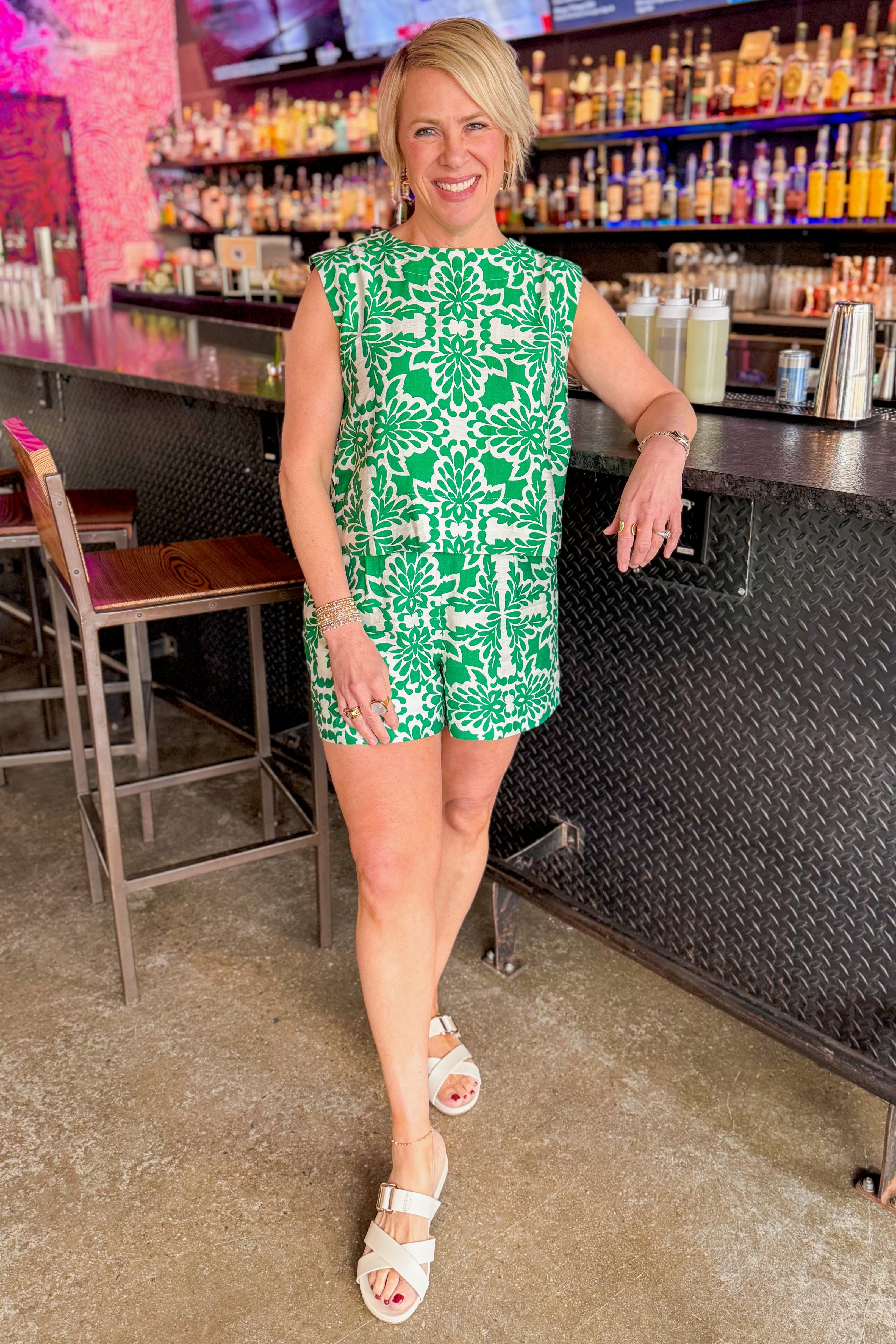 Front view of woman wearing Green &amp; Ivory Printed Tank by Skies Are Blue with matching shorts at a bar.