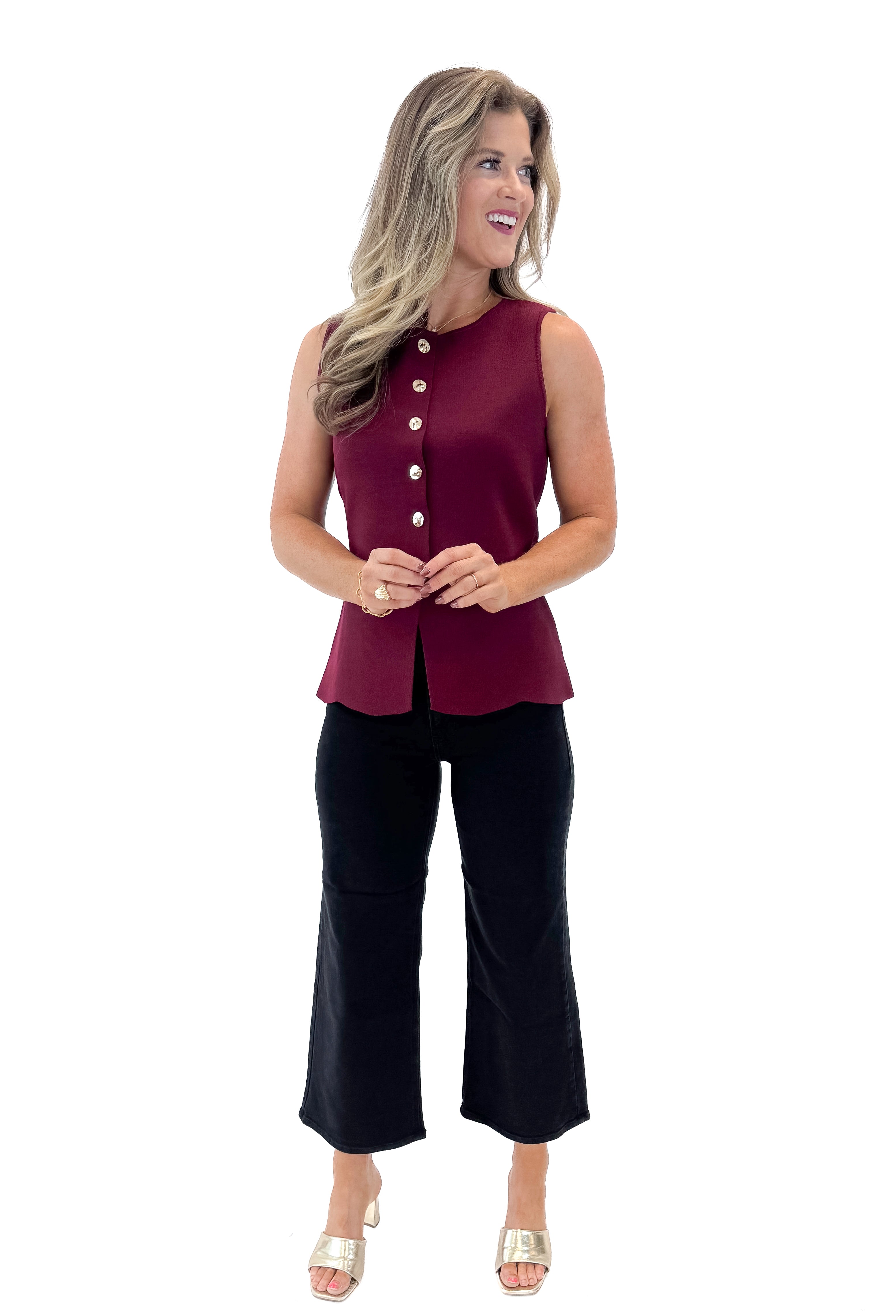 Front view of woman wearing Burgundy Button Detail Sleeveless Peplum Sweater with jeans against white studio background.