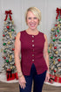 Front view of woman wearing Burgundy Button Detail Sleeveless Peplum Sweater with jeans with holiday decor.