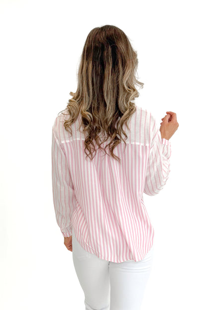 Back view of woman wearing Pink Striped Twist Top by Skies Are Blue with jeans against white studio background.