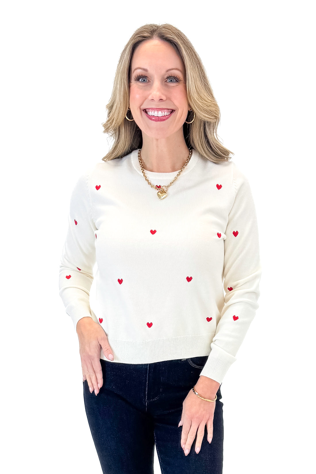 Front view of woman wearing White &amp; Red Embroidered Heart Sweater with jeans against white studio background.