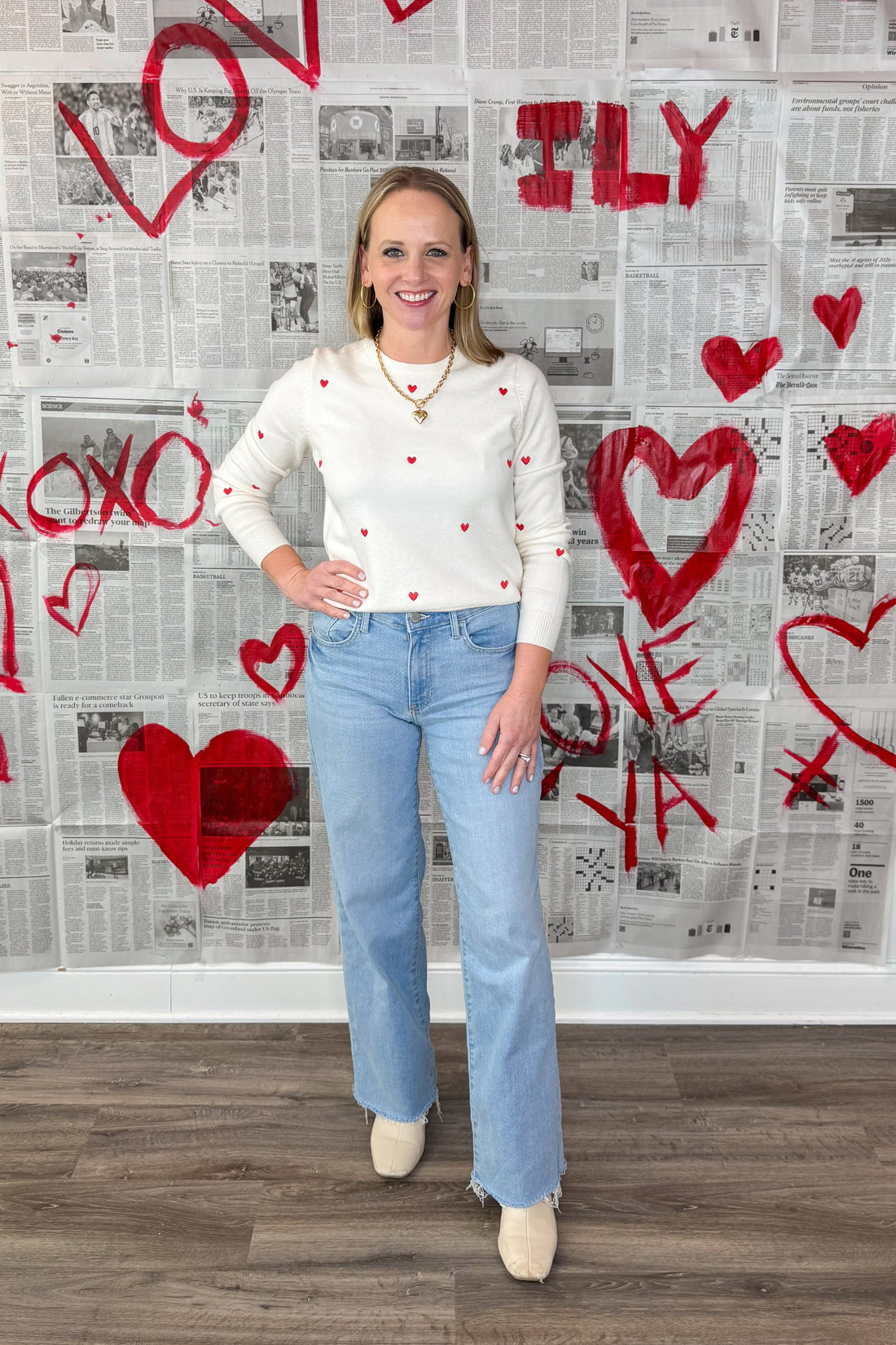 Front view of woman wearing White &amp; Red Embroidered Heart Sweater with jeans against Valentine&