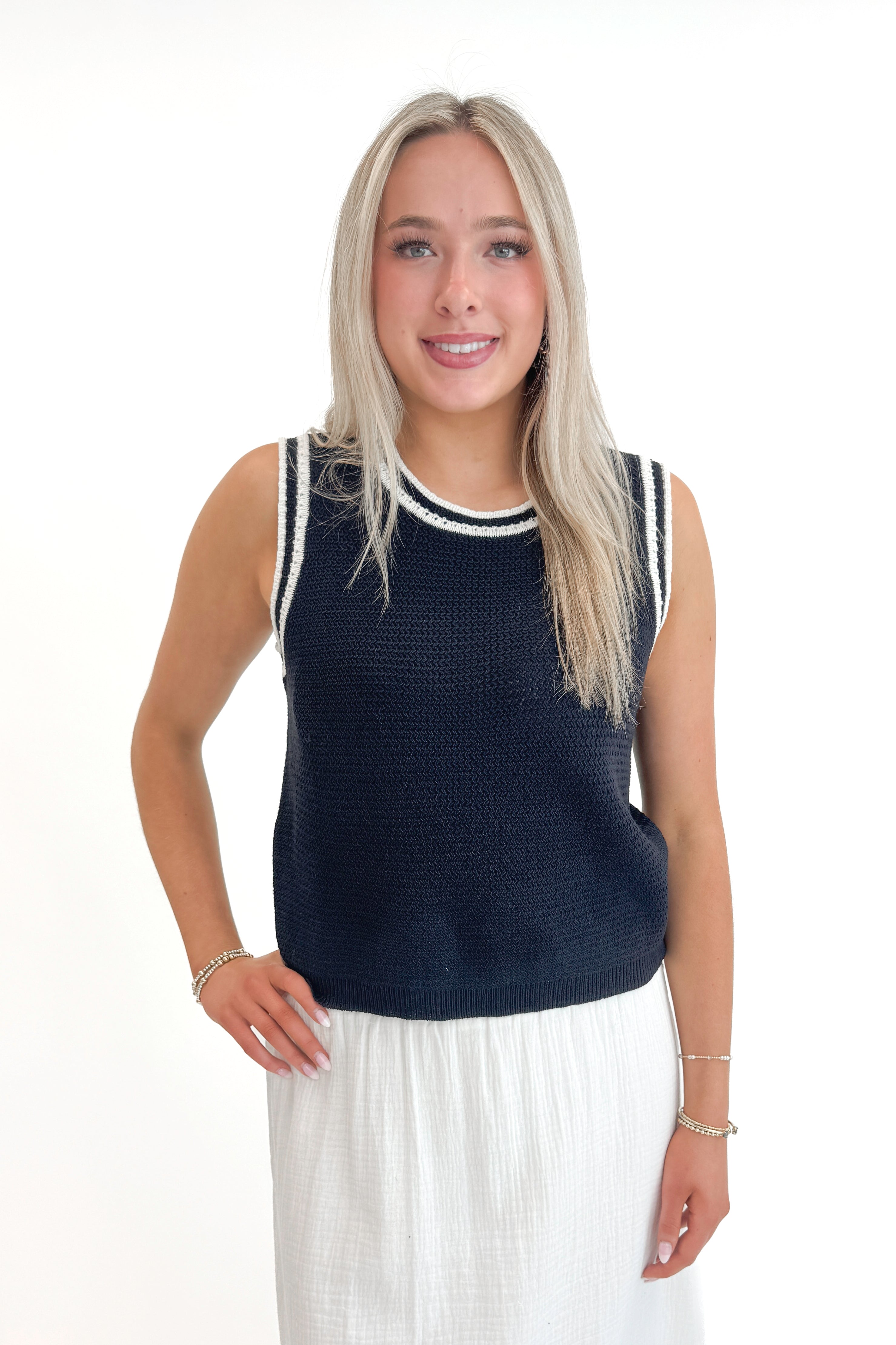 Front view of woman wearing Navy With White Lining Sweater Tank by Skies Are Blue with skirt against white studio background.