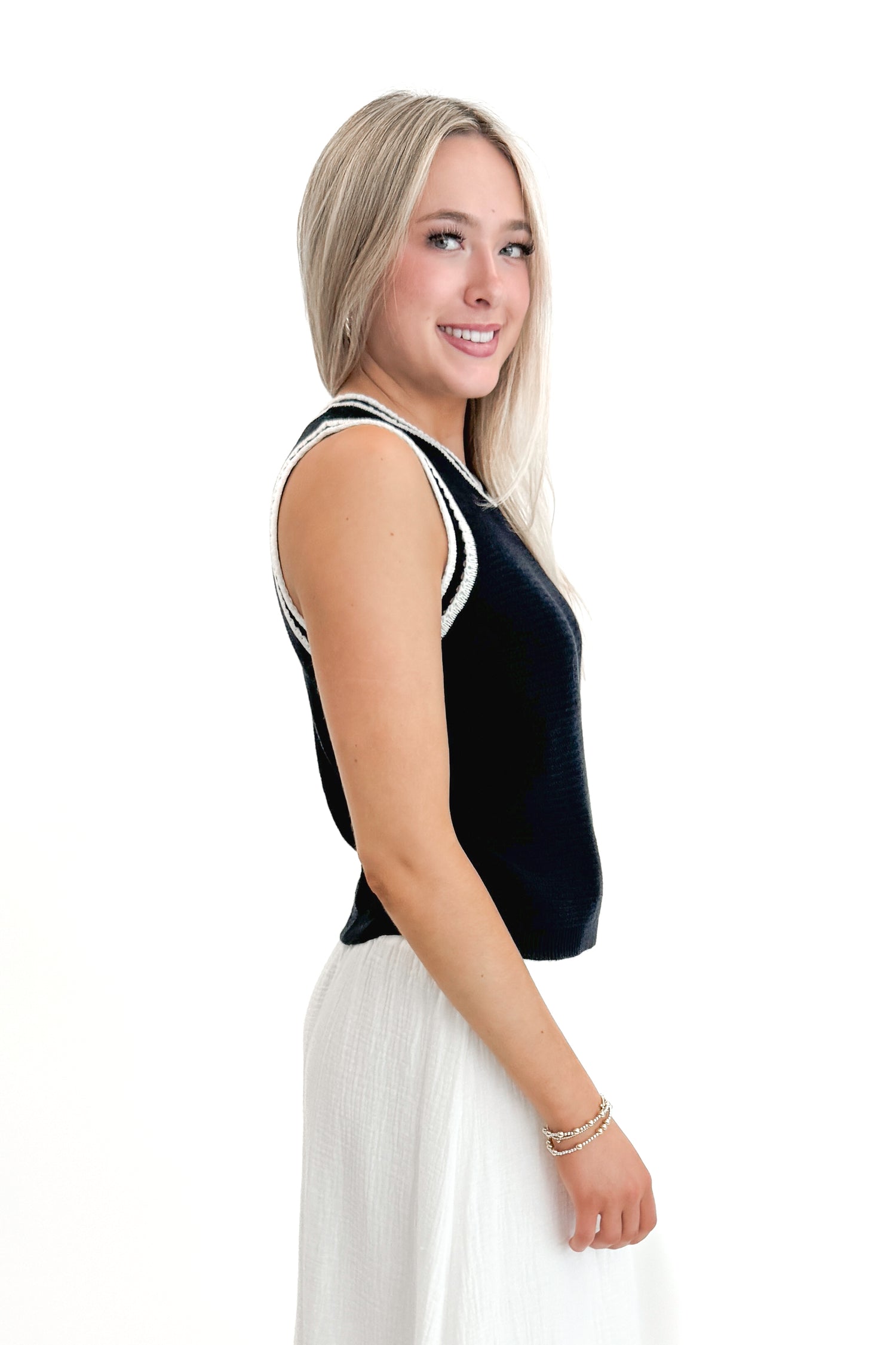 Side view of woman wearing Navy With White Lining Sweater Tank by Skies Are Blue with skirt against white studio background.