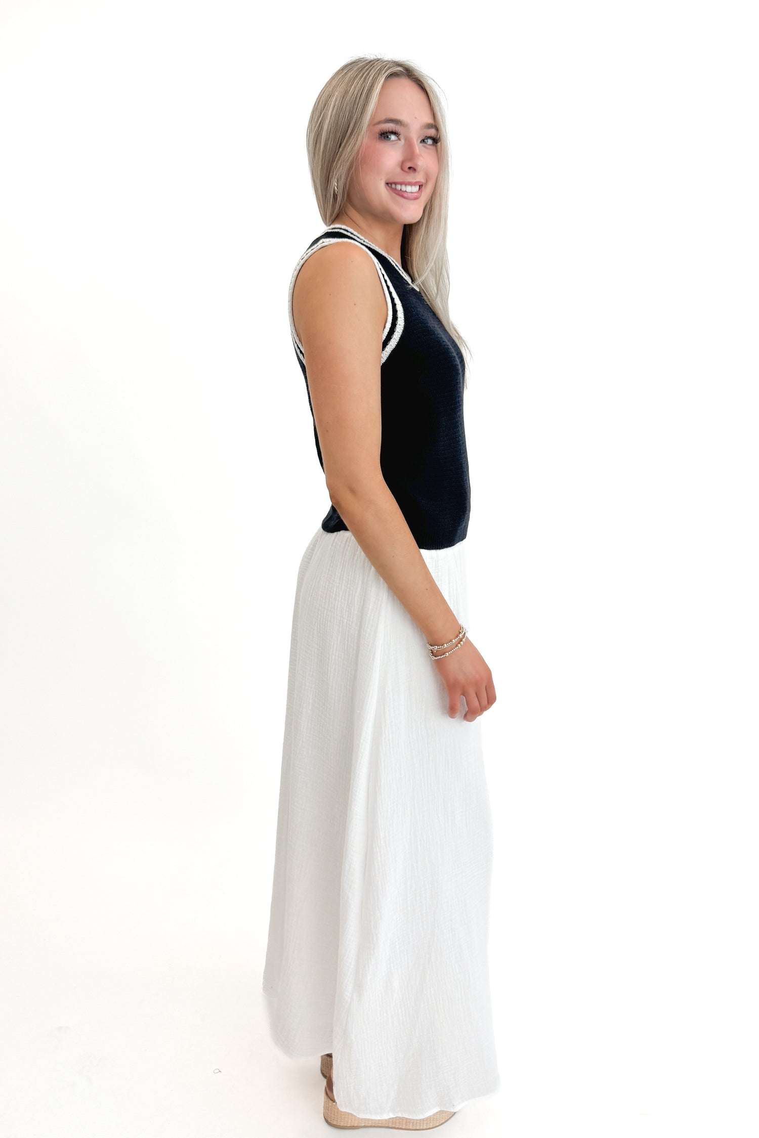 Side view of woman wearing Navy With White Lining Sweater Tank by Skies Are Blue with skirt against white studio background.