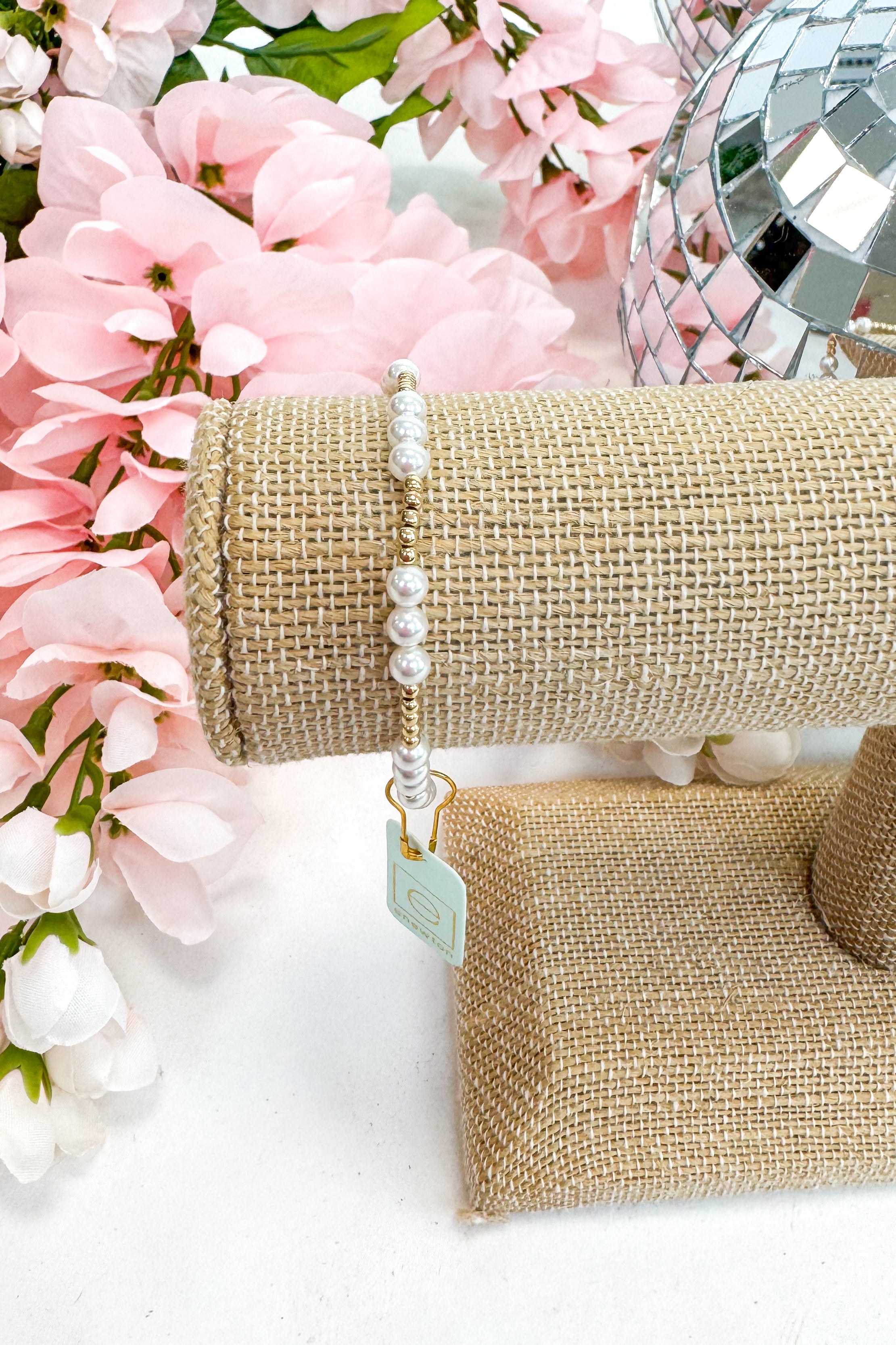 gold enewton bracelet with pearl detailing on burlap display with floral background