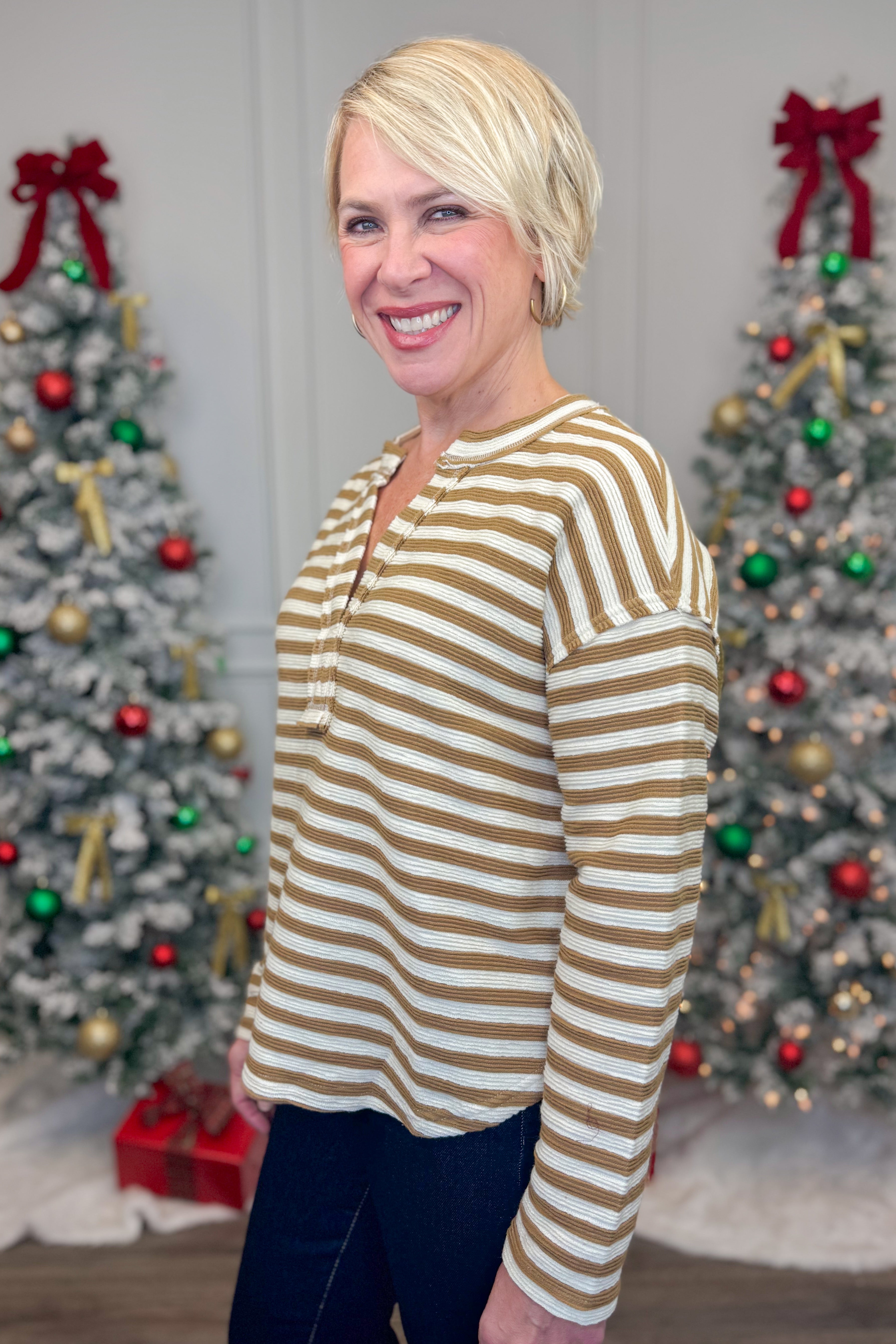 Woman in a striped shirt standing in front of two decorated Christmas trees.